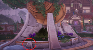 The picture shows the broken fountain in the cetner of Kilima Village and a red circle showing where the triangle is to interact with on the fountain to solve the part 2 riddle